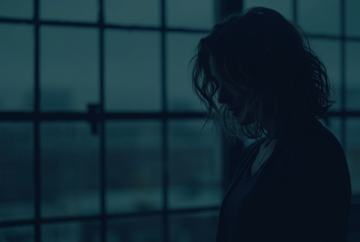 Silhouette of a woman turned toward soft light, standing quietly in shadow — a portrait of privacy and resolve.